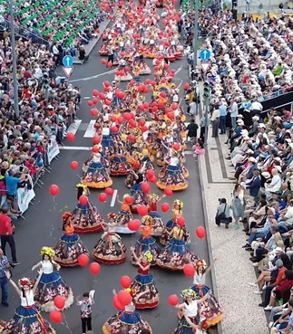 The Madeira Flower Parade from above – stands packed with spectators and a procession of dancers A drone shot showing the scale of the Flower Parade in Madeira – groups of dancers marching in rhythm, temporary stands packed with people, and the historic buildings of Funchal providing the backdrop to the event.