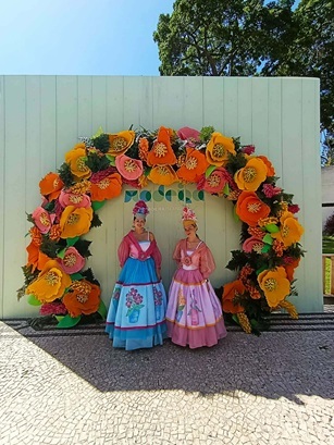 Women in traditional dress at the flower festival – Madeira in a decorative frame A framed photograph bearing the inscription "Madeira", showing a group of women in traditional floral costumes taking part in the Flower Festival in Madeira. The background features green foliage and colourful decorations.