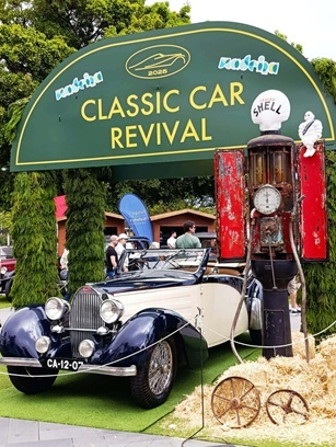 A vintage car at the entrance to the Vintage Car Parade in Madeira An old, vintage white car drives through the decorated entrance gate onto the grounds of the Vintage Car Parade festival in Madeira. In the background, the first groups of spectators and the island’s green landscapes can be seen.